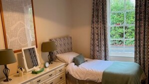 Un dormitorio con dos camas, un tocador, una mesita de noche, una lámpara y una ventana con cortinas.