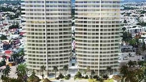 A high-rise hotel with multiple balconies, a swimming pool, and a landscaped area with palm trees. - Condos CAM (Mazatlán)
