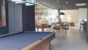 A billiards table in a modern indoor setting with wooden furniture and large windows. - Condos CAM (Mazatlán)