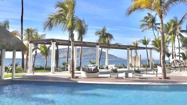 A poolside area with a pergola, lounge chairs, and palm trees. - Condos CAM (Mazatlán)