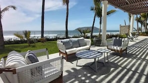 A covered outdoor seating area with a view of the ocean, furnished with a sofa, chairs, and a round table. - Condos CAM (Mazatlán)