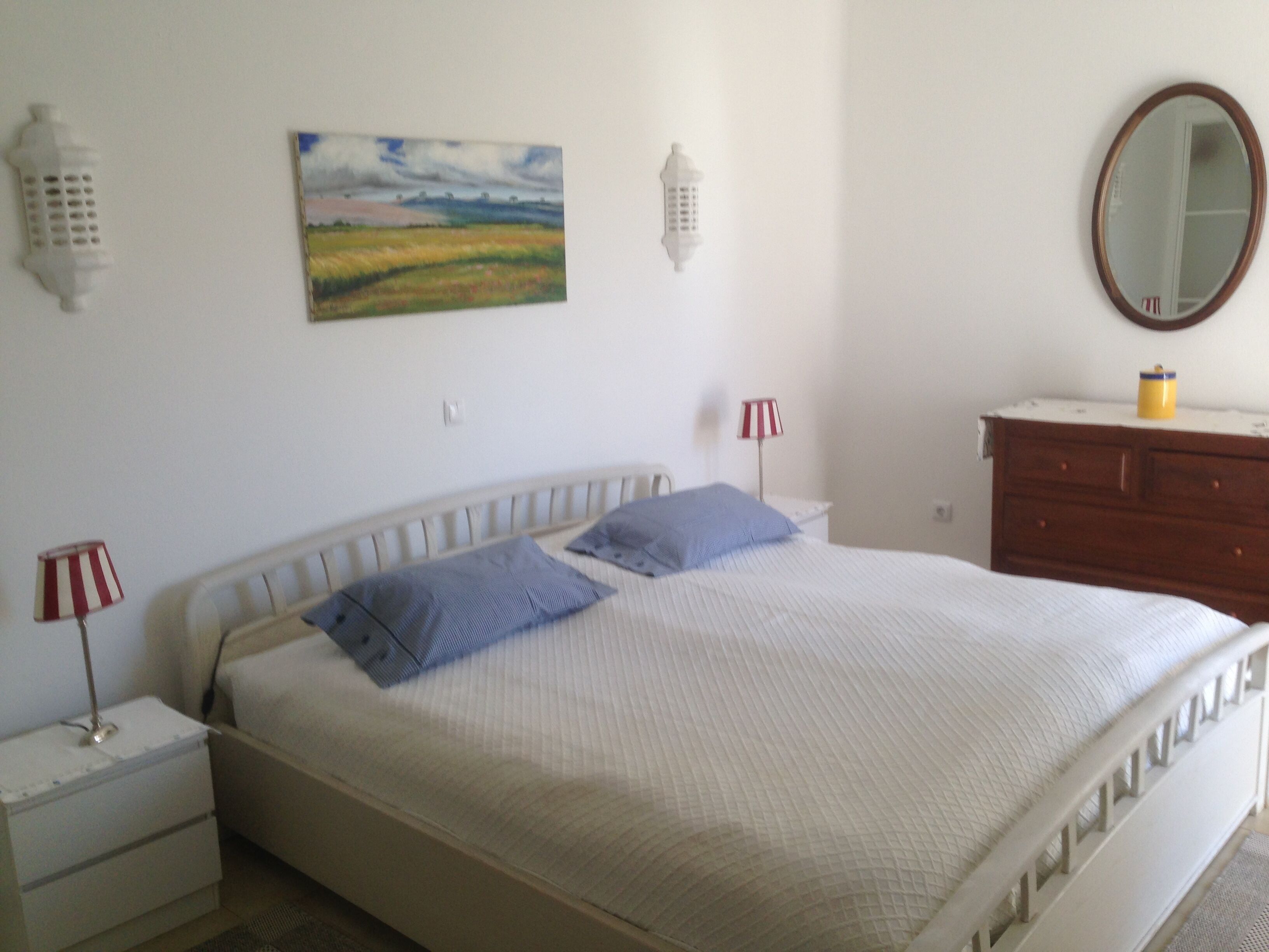 Ein Schlafzimmer mit Bett, Nachttischen, Kommode, Spiegel und einem Bild an der Wand.