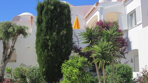 A white building with a dome and a chimney, surrounded by various plants and a yellow umbrella. - Quiet house with beautiful sea and country views Colina Branca 10 (Carvoeiro)