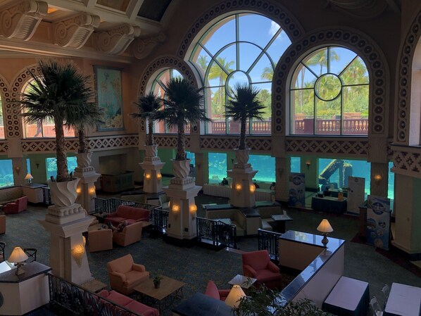A spacious lobby with high ceilings, large arched windows, and palm trees.