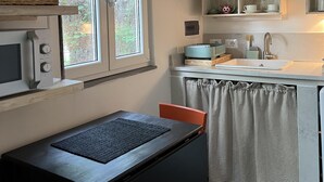 A kitchen with a microwave, sink, and cabinets. There is a window with a view of trees. - A cottage in the middle of the countryside just a stone's throw from the center of Florence<br> (Toscana)