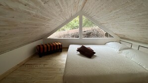 A bedroom with a sloped ceiling, a large window, a bed with pillows, and a striped bench. - A cottage in the middle of the countryside just a stone's throw from the center of Florence<br> (Toscana)