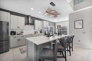 Una cucina moderna con mobili bianchi, un'isola grande e un'area da pranzo con sedie rivestite di grigio.