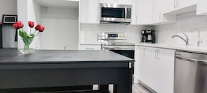 Una cocina moderna con armarios blancos, electrodomésticos de acero inoxidable y encimera negra.