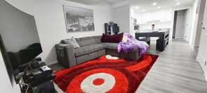 Una sala de estar moderna con un sofá seccional gris, un tapete rojo y blanco, y una pintura de un paisaje urbano en la pared.