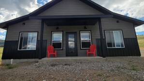 A two-story house with a dark exterior, a front porch with two red chairs, and large windows. - Beautiful brand new house with breathtaking Shining Mountain views. (Ennis)