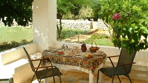 Mesa al aire libre con sillas, piso de piedra y vista a un jardín.