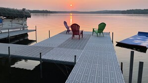 Eine Anlegestelle mit zwei Stühlen, die den Sonnenuntergang über einem ruhigen See hinweg zeigen.