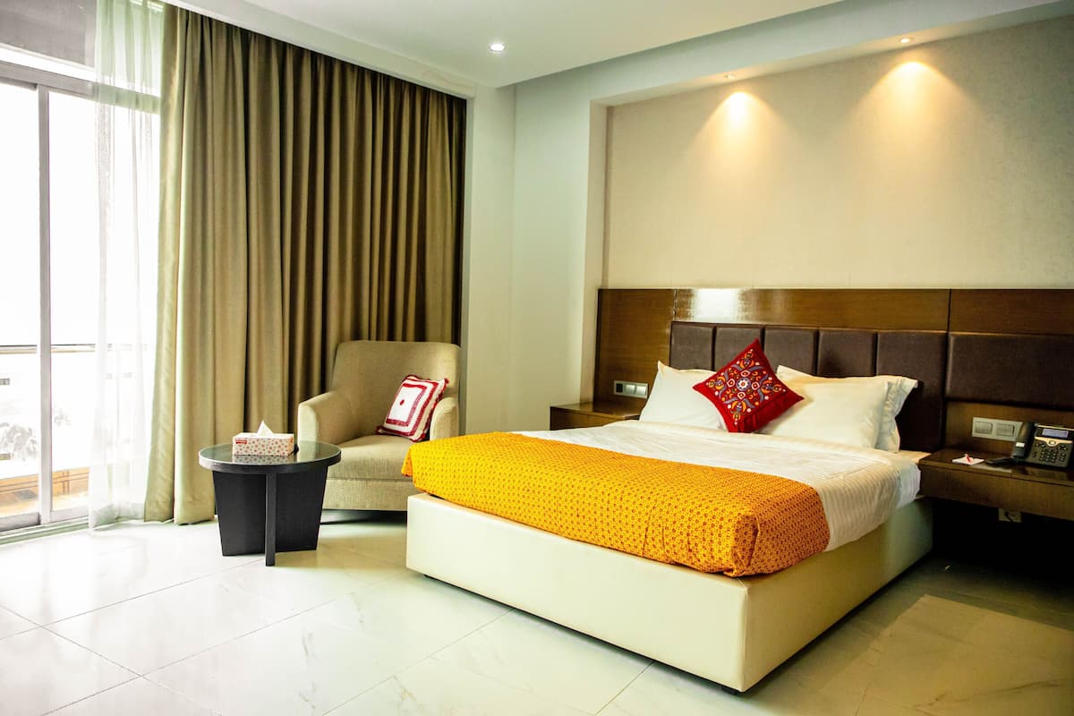 A hotel room with a large bed, a chair, a small table, and a nightstand with a phone.