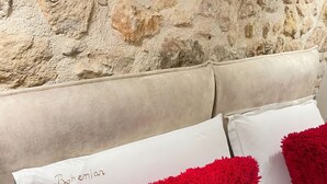 A bed with white pillows and red throw pillows against a stone wall. - Bohemian Boutique Suites (Vlorë)