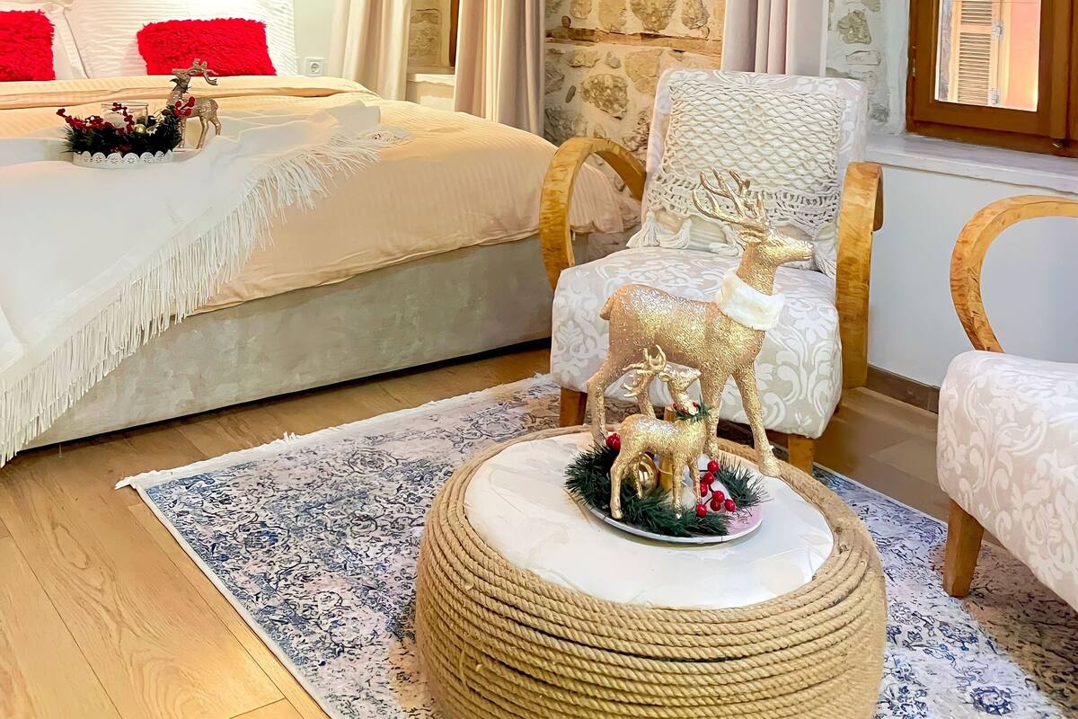 A cozy bedroom with a bed, two chairs, a round coffee table, and a stone wall.