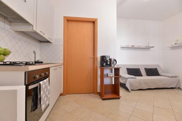 Una cocina compacta con estufa, horno y lavamanos, una puerta de madera, un sofá y un estante con cafetera.