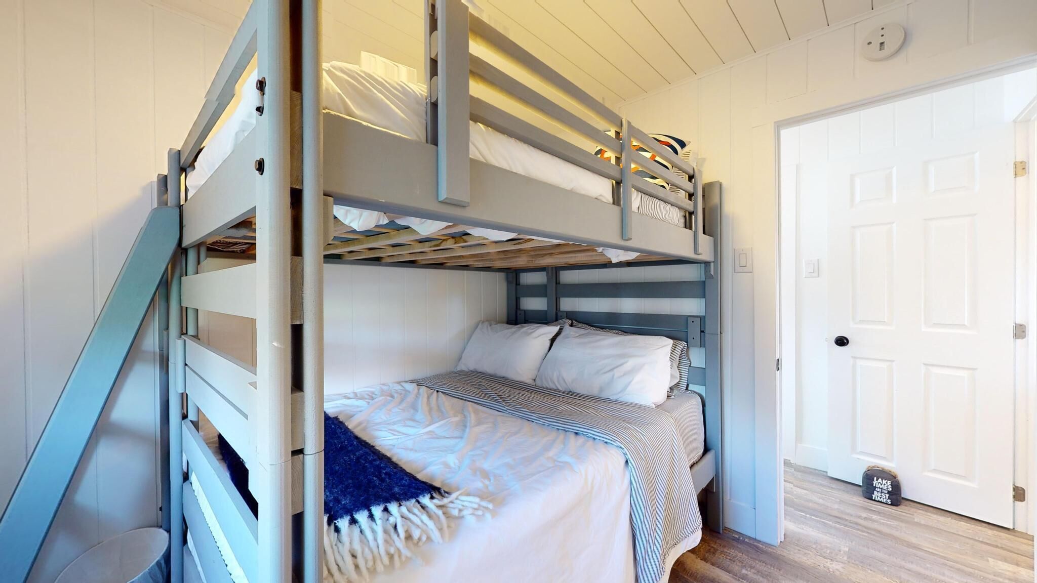 A bunk bed room with a wooden ladder, a white door, and a small rug on the floor.