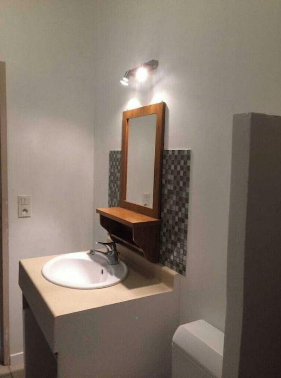 A bathroom with a white sink, a wooden vanity, a mirror, and a tiled backsplash.