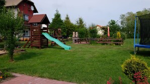 Une aire de jeux avec un toboggan et des balançoires, entourée d’une pelouse et d’arbres.