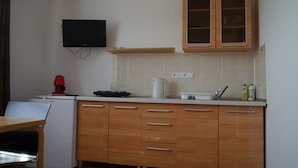 Une cuisine compacte avec des meubles en bois, un four à micro-ondes encastré, un petit réfrigérateur, une machine à café et un téléviseur fixé au mur.