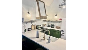 A kitchen with white countertops, green cabinets, a hanging light fixture, and a white refrigerator. - Cozy Mountain Cabin Perfect for Families and Pets (Franklin)