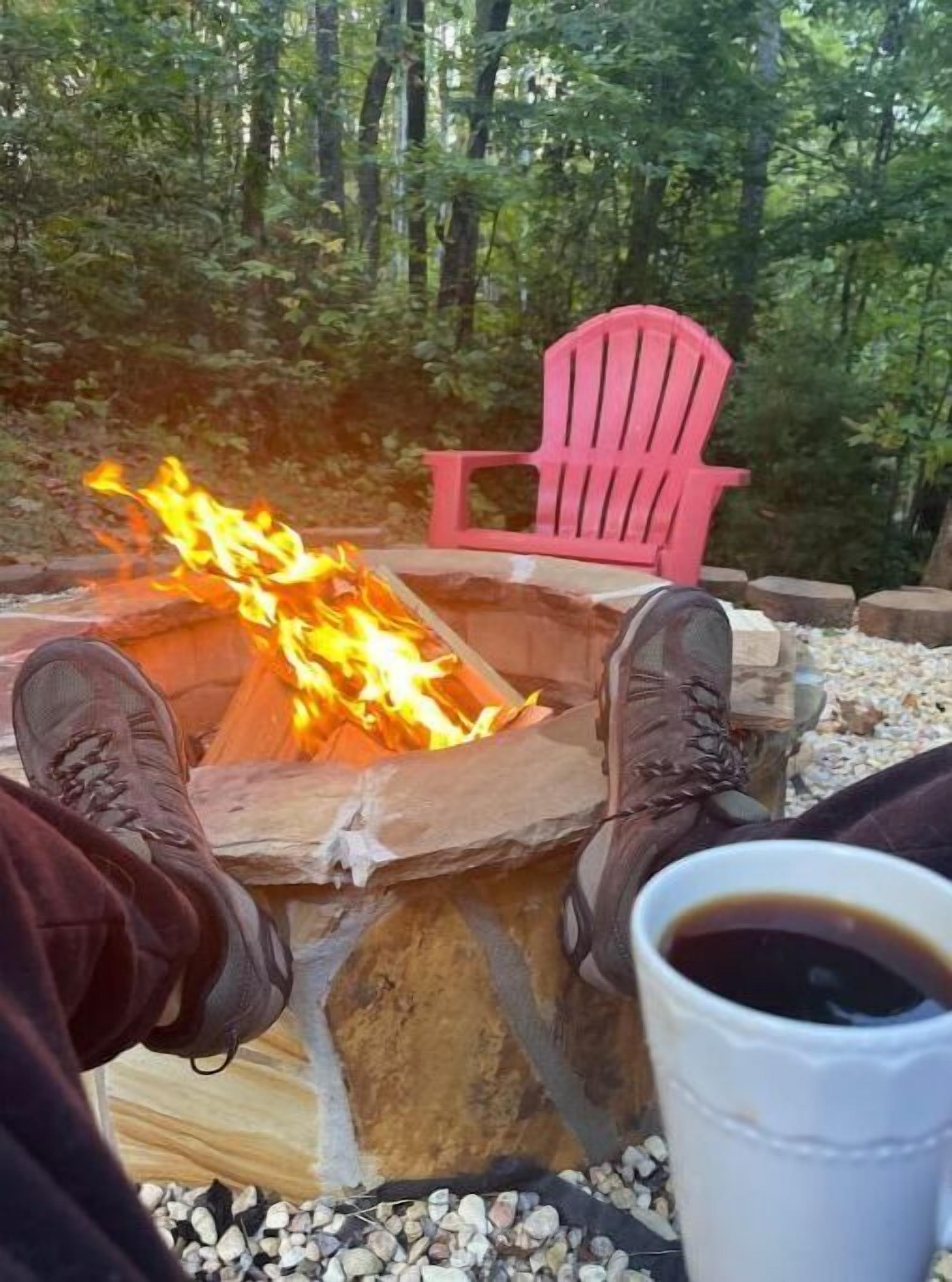 A campfire with logs, a red chair, and a cup of coffee.