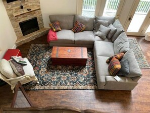 Een woonkamer met een grijze modulaire bank, een houten salontafel, een vloerkleed met dessin en een open haard.