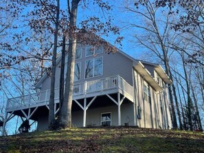 Une maison à deux étages avec un balcon au deuxième étage, entourée d’arbres.