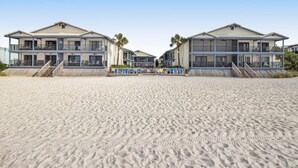Een hotel aan het strand met gebouwen van twee verdiepingen, een zandstrand ervoor en een heldere lucht.