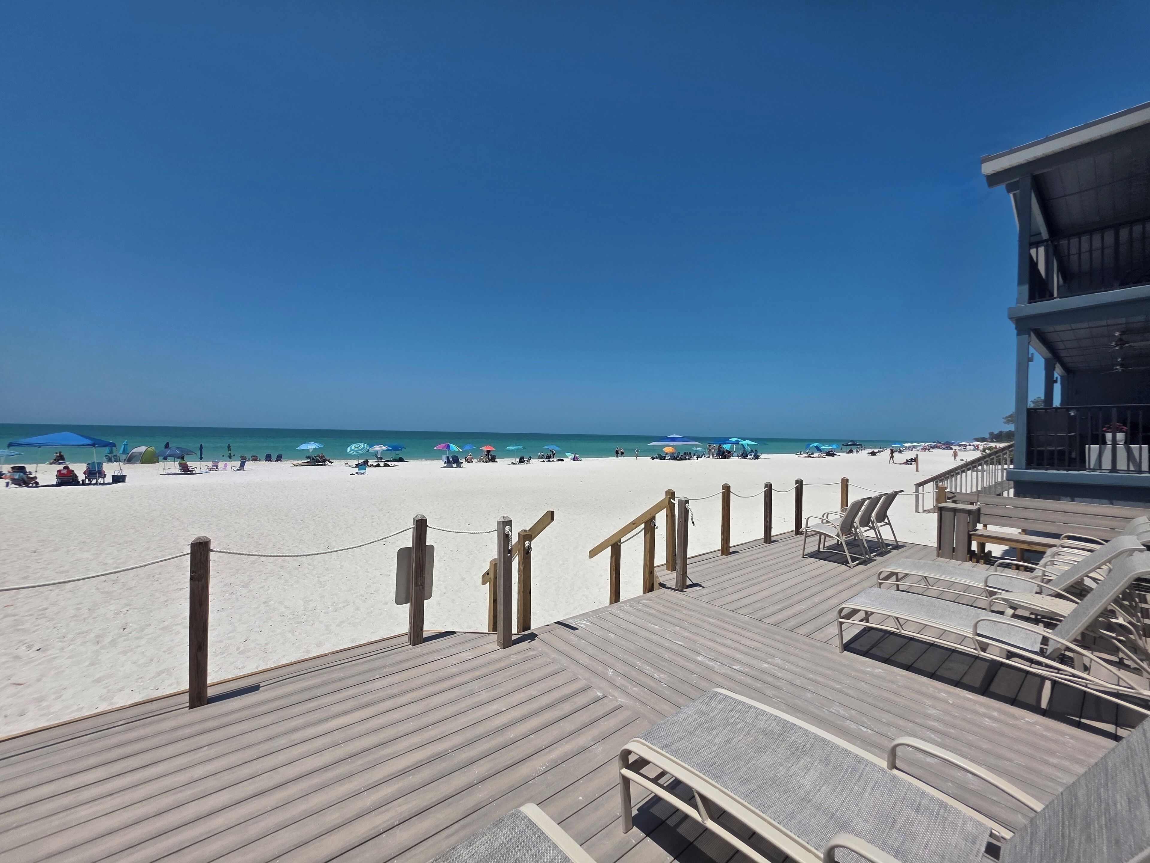 A beach view from a wooden deck with lounge chairs and a lifeguard tower.