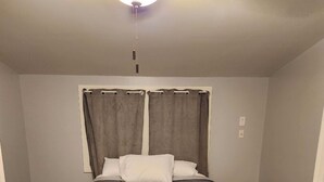 Un dormitorio con una cama, un ventilador de techo y un altavoz negro pequeño.