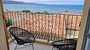 Un balcón con vista al mar, dos sillas de mimbre y un tejado de baldosas.