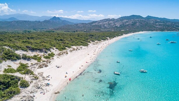 Vista aérea de una zona costera con playa de arena, aguas turquesas cristalinas y embarcaciones.