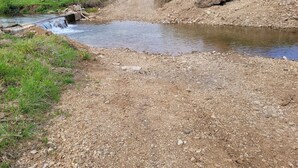 Un sentier de gravier mène à un petit ruisseau qu'enjambe un pont en bois.