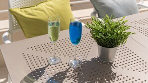 Ein Balkon mit Tisch, zwei Stühlen, einem Blumentopf und zwei Getränken.
