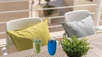 Un balcon avec une table, deux chaises, une plante en pot et deux boissons.