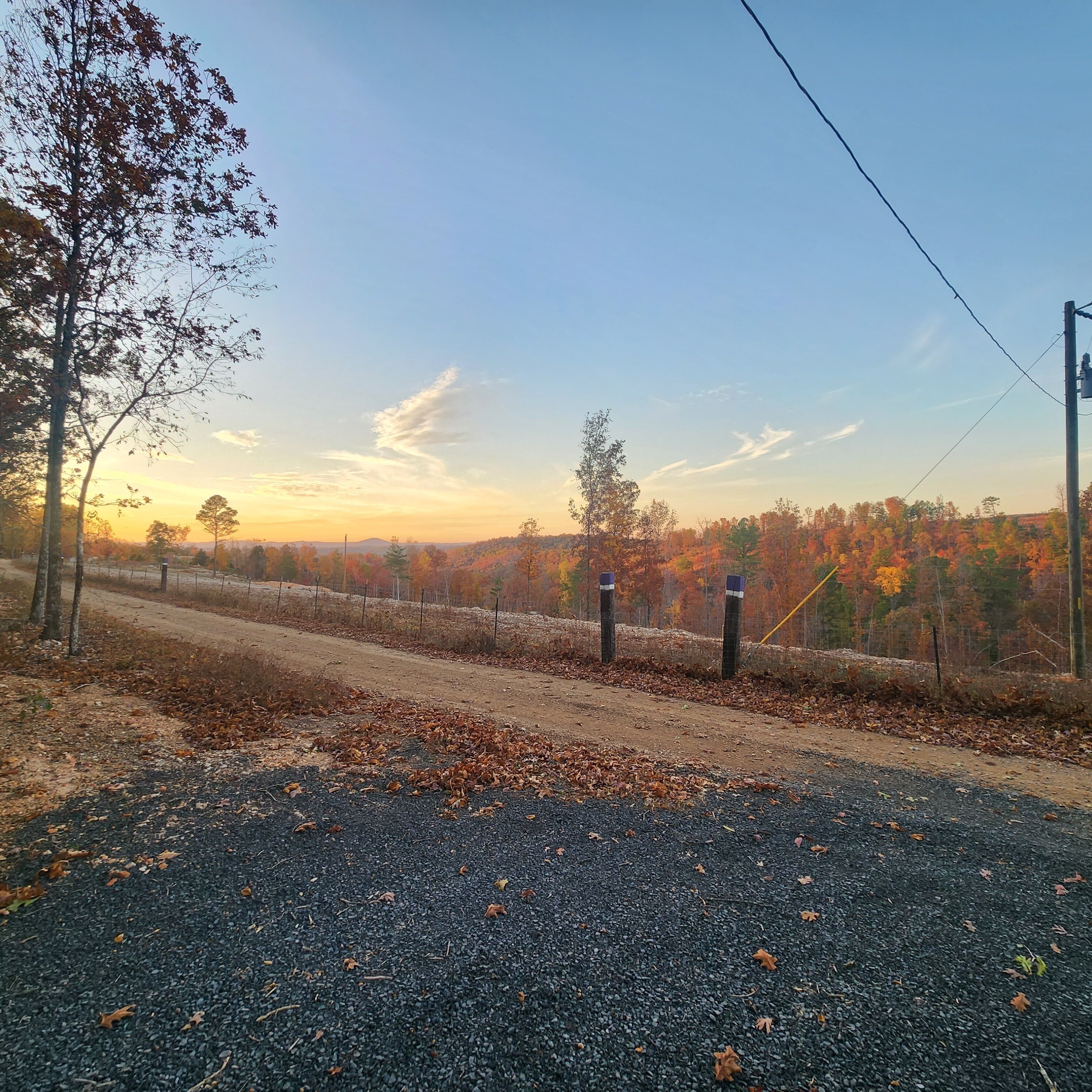 A gravel road with trees and a fence in the background.