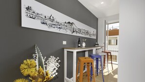 A modern kitchen with a white countertop, a hanging black and white cityscape painting, and a vase with yellow flowers. - Vivaldo Suite - Piazza dei Martiri (Naples)