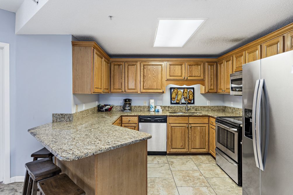 A kitchen with wooden cabinets, a granite countertop, stainless steel appliances, and a small island with stools.