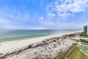 A beach view with a sandy shore, a clear blue sky, and a building in the background.