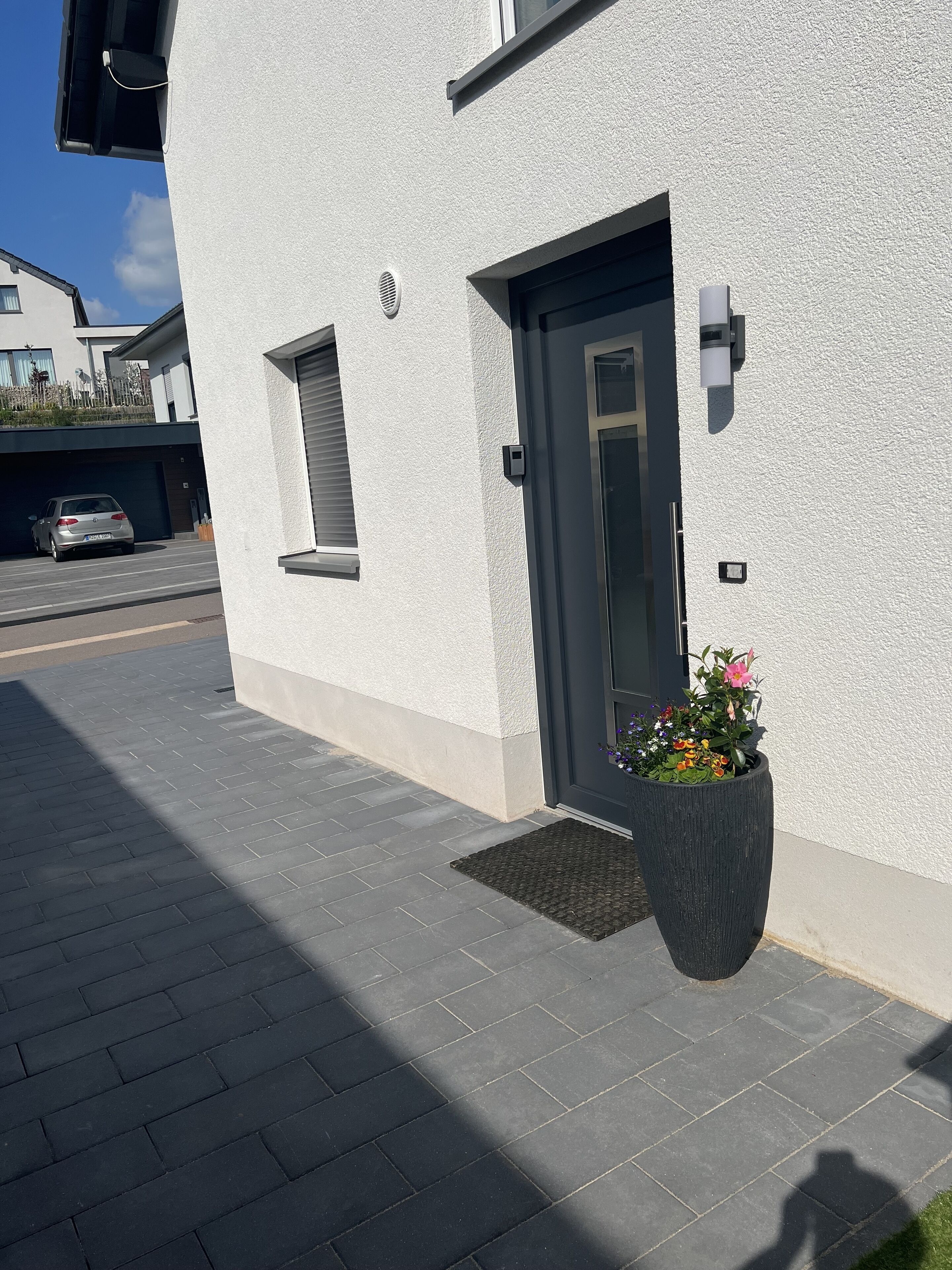 Un bâtiment moderne à l’extérieur blanc, avec une porte d’entrée sombre et un grand bac à fleurs.