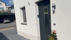 Un edificio moderno con facciata bianca, porta d'ingresso scura e un grande fioriere con fiori.