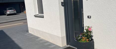 Un bâtiment moderne à l’extérieur blanc, avec une porte d’entrée sombre et un grand bac à fleurs.