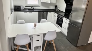 Una cucina compatta con mobili bianchi, un frigorifero in acciaio inossidabile, un forno a microonde e una finestra con vista sulla strada.