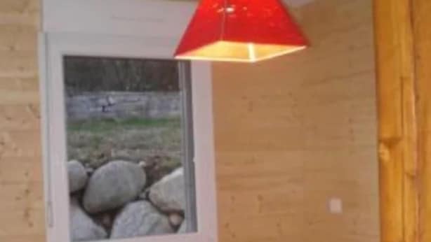 Une chambre avec un lit, une fenêtre donnant sur des rochers et une lampe suspendue rouge.