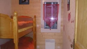 Une petite pièce avec un lit superposé, une fenêtre ornée d’un rideau rouge et une porte.