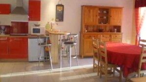 Une cuisine avec des meubles de rangement rouges, une table à manger avec des chaises et un buffet en bois avec des portes en verre.
