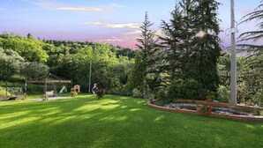 Un jardín bien cuidado con un porche estilo pagoda, un conjunto de columpios y un macetero de ladrillo con flores.