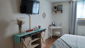 A bedroom with a bed, a desk with a mirror, a TV mounted on the wall, and a window with curtains.