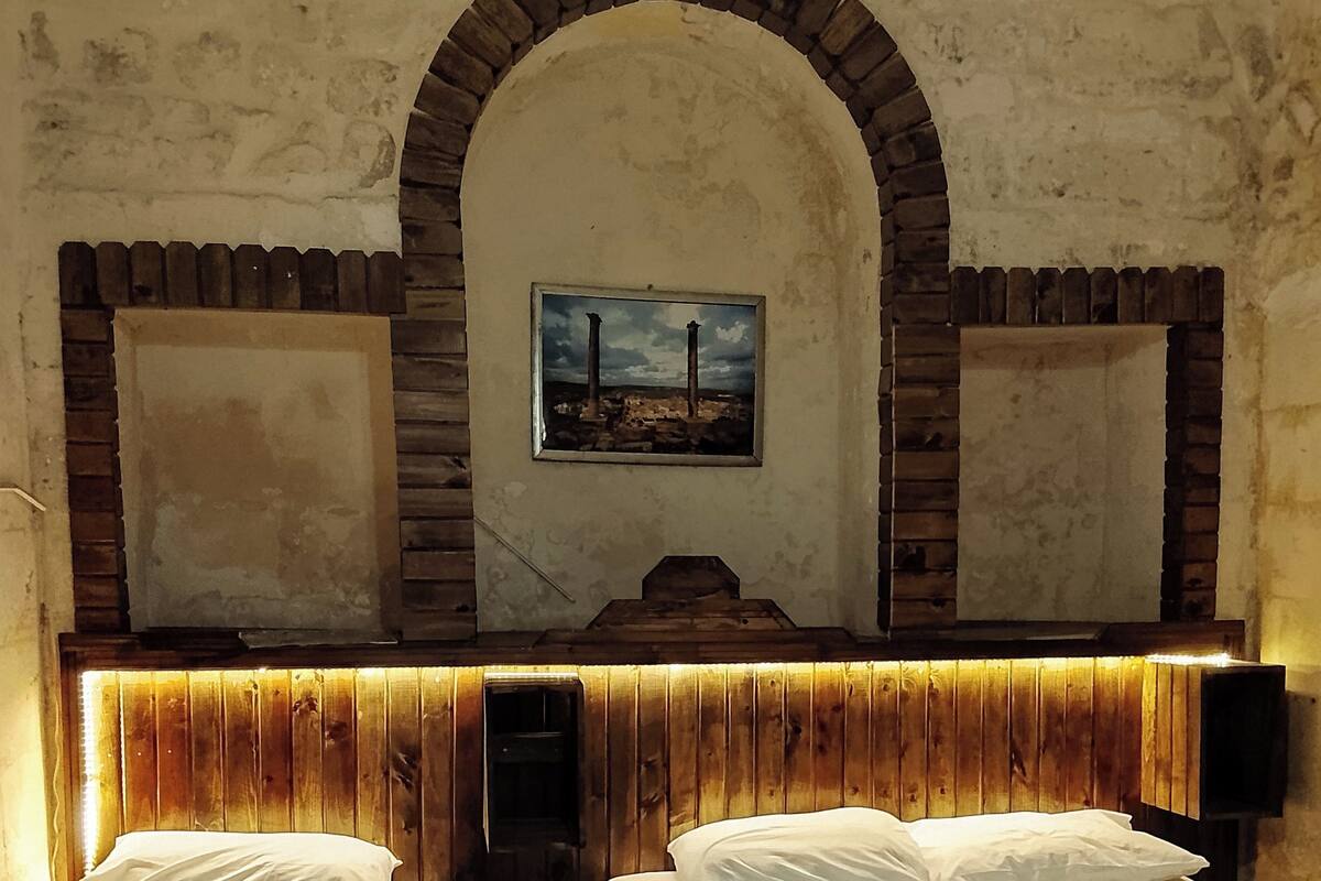 A room with two beds, wooden paneling, a painting of ruins, and a brick archway.